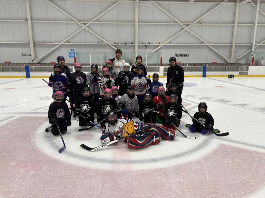 Jeunes joueurs et entraîneurs AHMV réunis pour une photo de groupe sur la glace.